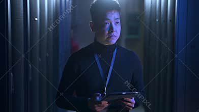 Male engineer using device and checking equipment racks while walking in data center spbas.