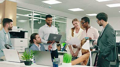 A closer angle of a blonde woman in a suit walks into a large aesthetic office, she talks to some of the people from the