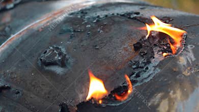 The skin on the metal of the damaged vehicle is burning. Open fire close-up with wiring. Detail of charred wreckage.