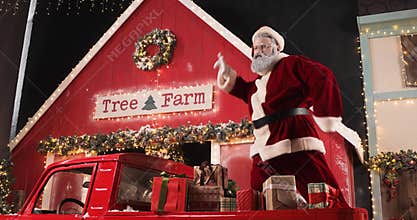 Funny Santa Claus is dancing in a New Year's decorated studio in a red truck with New Year's gifts near a Christmas tree