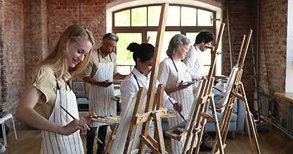 Different age and ethnicity people painting on easel during class