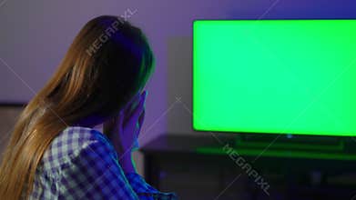 Young woman sits on an armchair and watches TV. Remote controller.