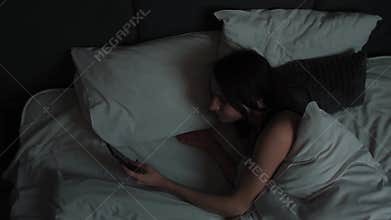 Beautiful Girl Sleeping in Bed at Home Wakes Up to Disable Alarm Clock Triggered on Her Phone and Turns Away to Sleep in