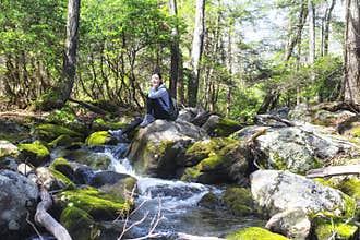 Chinese woman sitting on rocks near a new england stream