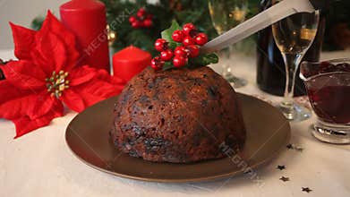 Woman hand cut a Christmas pudding with holly on top.