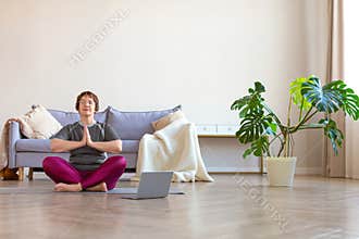 An elderly woman practices yoga. Home workouts led by an online instructor.