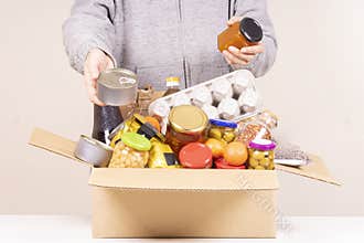 Volunteer hands with food donation box full of grocery products on white desk
