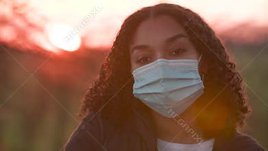 Mixed race African American girl biracial teenager teen young woman outside putting on a face mask during COVID-19 Coronavirus pan
