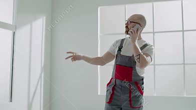 Builder in jumpsuit calls on mobile phone in empty room