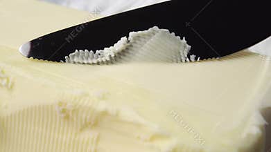 Farm butter is cut with a serrated knife in a thin layer close up