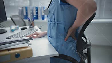 backache close up, female doctor in blue uniform working at the computer suddenly felt pain in the back and lower back