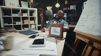 Cheerful African American businessman fanning face with cap in late coworking.