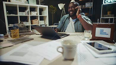 Smiling African businessman talking cellphone in dark coworking.