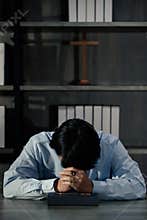 Asian man bowing his head on the Bible and carrying a cross. According to the beliefs of Christianity Is the salvation of Jesus.