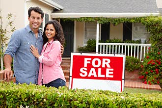 Hispanic couple satnding with a sign outside house