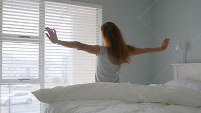Beautiful girl Slowly Waking up in the Morning, Stretches and Gets Up from the Bed, Sun Shines on Her From the Big