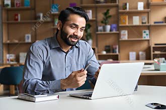Young indian business man talking, having virtual meeting working on laptop.