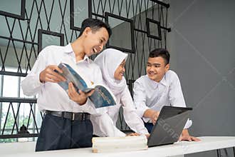 three Asian teenagers study together in school uniforms to chat while using a laptop and several books