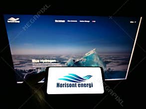 Person holding mobile phone with logo of Norwegian carbontech company Horisont Energi AS on screen in front of web page.