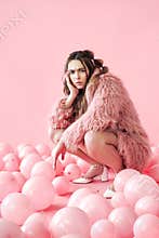 Serious hipster woman sitting in many pink balloons background