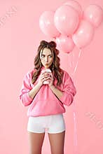 Trendy young woman drinking milk shake over pink balloons background.