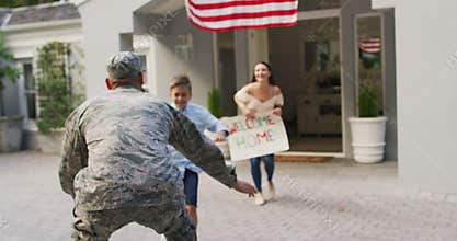 Caucasian male soldier greeting happy son and wife with welcome home sign outside their house