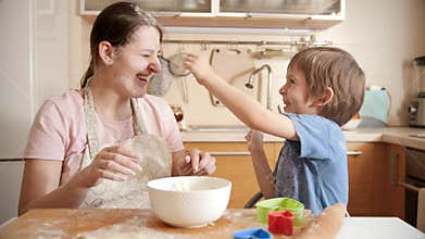 Laughing mother with son throwing flour at each other while cooking at home. Children cooking with parents, little chef