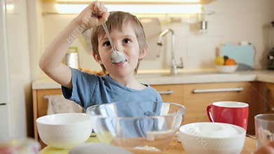 Happy smiling little boy eating ingredients for cooking and baking pie with spoon. Children cooking with parents, little