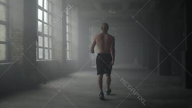 Man silhouette walking in dark corridor. Athlete taking break after workout