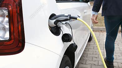 Man coming to the electric car and plugging in a charging cable.