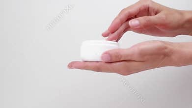 Woman's hands applying cream in a white jar, on a white background