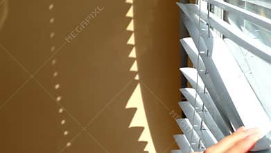 Window with closed blinds. Arm comes into frame and opens blinds to look outside. The concept of spying on neighbors.