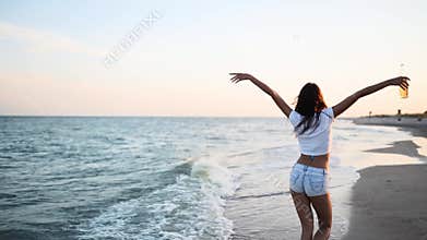 Pretty woman walking along seaside on a sandy beach having fun with beer bottle. Attractive fitted girl sends air kiss