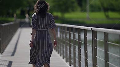 lonely woman is walking on bridge over river at summer day, rear view