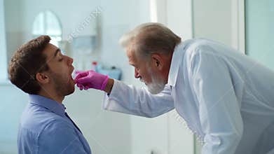 Mature male doctor testing sick young man patient for for possible coronavirus infection using throat swab during