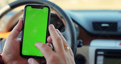 Man hand using chromakey mobile phone with empty green screen in modern car. Mockup touchscreen. internet searching.