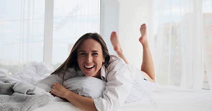 Beautiful young woman hugging pillow while lying on bed