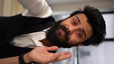 Vertical POV portrait of cheerful Indian bearded businessman talking to colleagues via video call using mobile phone