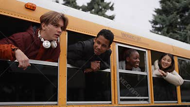 Joyful teens with heads out of school bus windows