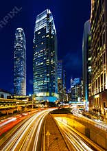 Rush hour traffic light trails lead to tall vertical skyscrapers in Hong Kong downtown