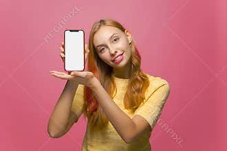 Smiling beautiful girl showing phone with empty blank mock-up screen, advertising new apps on pink studio background