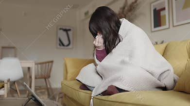 Cold young woman talking with doctor through a video call with a laptop at home