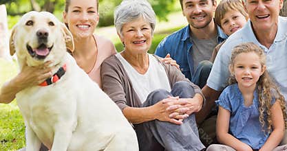 Portrait of happy caucasian multi generation family sitting with pet dog in park