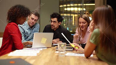 Young creative multi-ethnic business team discussing startup project sitting at desk with laptop in meeting room.