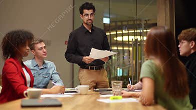 Multiethnic startup business team sitting at table listen to report of colleague making speech at group meeting briefing