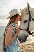A young woman and a white horse against the background of the sky and the sea.