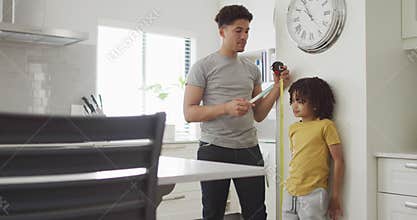 Happy biracial man and his son measure height in kitchen