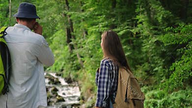 Backpacking tour in woodland, man and woman are viewing waterfall