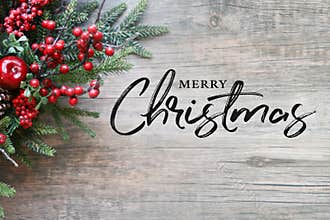 Merry Christmas Text with Christmas Evergreen Branches and Berries in Corner Over Rustic Wood Background