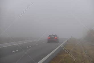 Cars in the fog. Bad winter weather and dangerous automobile traffic on the road. Light vehicles in fog